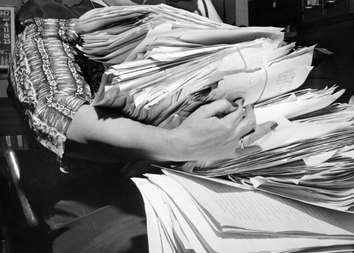 Archive photograph of hands sorting through a tall stack of handwritten papers